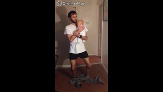 Папа надевает штаны с малышом на руках